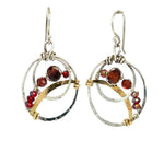 A pair of handmade petite double hoop earrings with red tiger's eye and garnet gemstones, set in hammered brass arches with sterling silver French hooks.