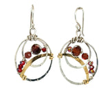 A pair of handmade petite double hoop earrings with red tiger's eye and garnet gemstones, set in hammered brass arches with sterling silver French hooks.