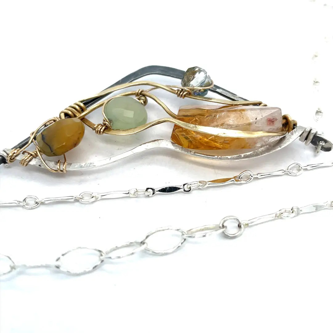 An oxidized sterling silver wedge pendant with waves of hammered sterling silver and brass wires, mixed with citrine, jade, crystal, and yellow opal gemstones to form this gemstone wedge necklace
