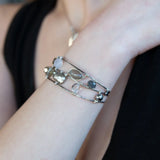 A collection of labradorite, purple blue fresh water pearl, green crystal, and quartz gemstones on a dandelion stamped oxidized sterling silver wide cuff bracelet