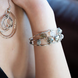 A collection of labradorite, purple blue fresh water pearl, green crystal, and quartz gemstones on a dandelion stamped oxidized sterling silver wide cuff bracelet