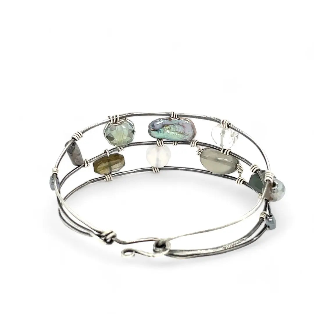 A collection of labradorite, purple blue fresh water pearl, green crystal, and quartz gemstones on a dandelion stamped oxidized sterling silver wide cuff bracelet