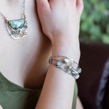 A collection of labradorite, purple blue fresh water pearl, green crystal, and quartz gemstones on a dandelion stamped oxidized sterling silver wide cuff bracelet