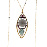 A necklace with a brass keyhole pendant containing a tapestry of smokey quartz, faceted garnet, and a marquise London blue quartz gemstone, attached to a delicate gold filled chain