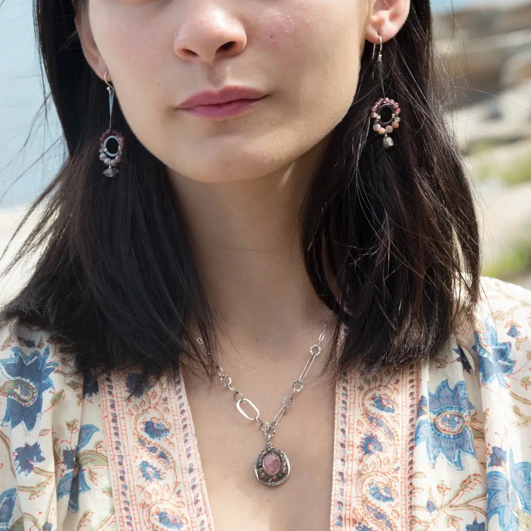 Darkened sterling silver ring surrounded by pink tourmaline and opal gemstones with a herkimer diamond dangle, attached to a darkened sterling silver twisted bar top earring