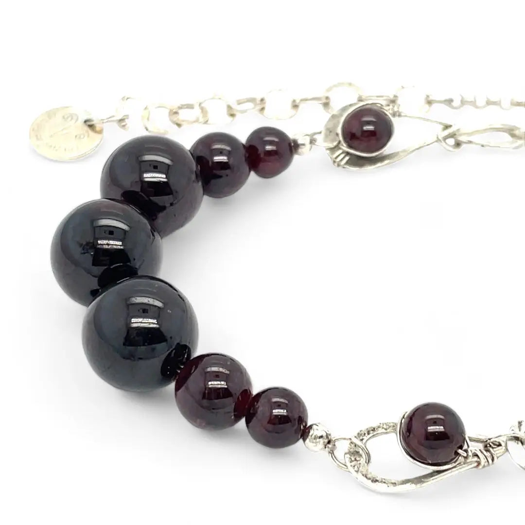 Smooth garnet sphere gemstones are suspended between handmade sterling silver hammered teardrops on sterling rolo chain necklace