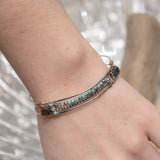 A sterling silver cuff bracelet featuring labradorite luster faceted gemstone cubes, and lines of mint crystal and pyrite, displayed on a sterling silver cuff bracelet