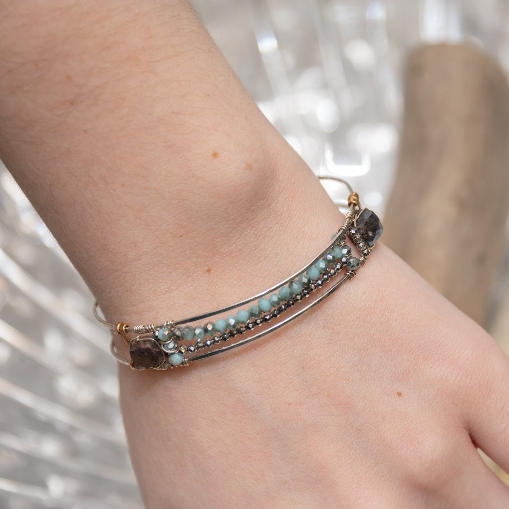 A sterling silver cuff bracelet featuring labradorite luster faceted gemstone cubes, and lines of mint crystal and pyrite, displayed on a sterling silver cuff bracelet