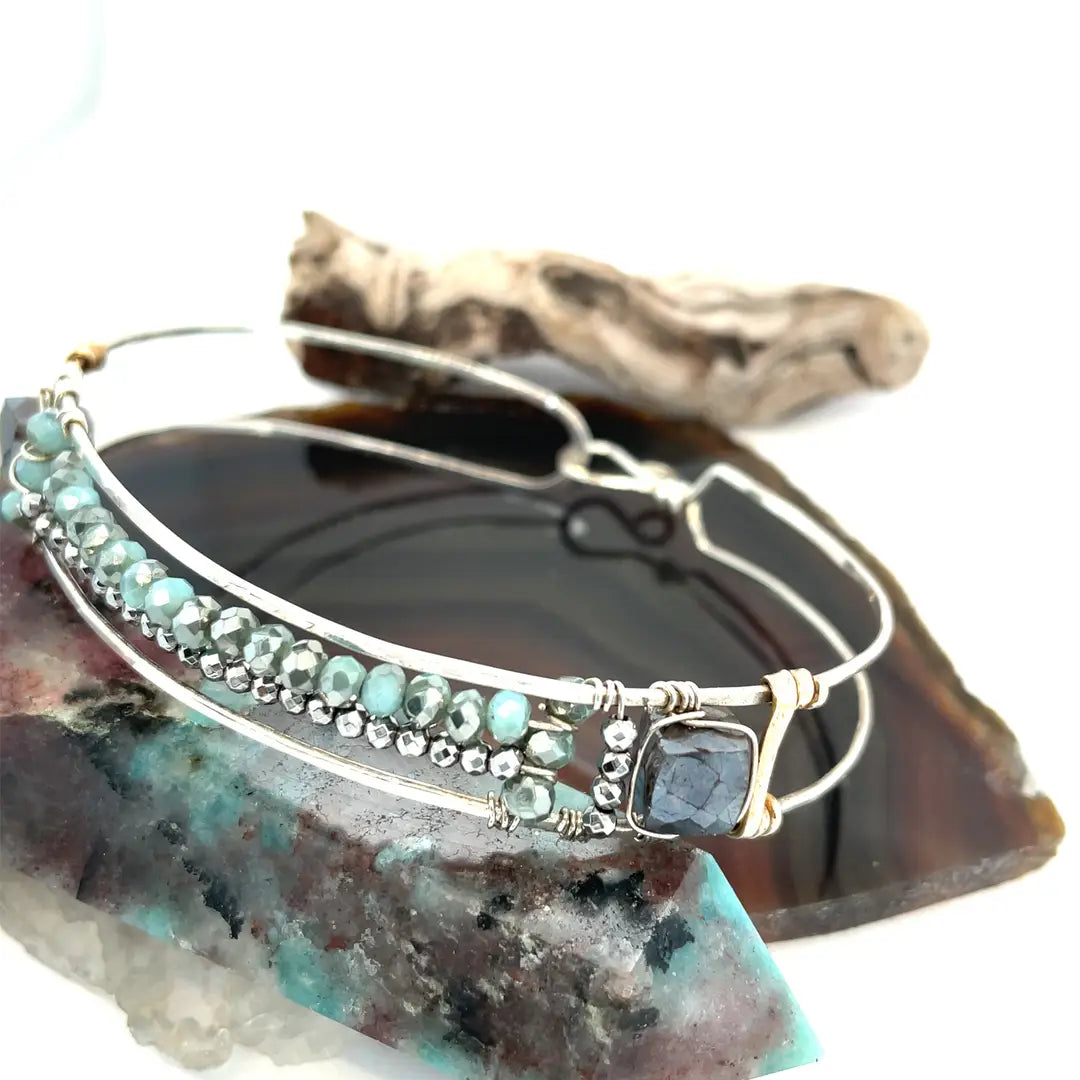 A sterling silver cuff bracelet featuring labradorite luster faceted gemstone cubes, and lines of mint crystal and pyrite, displayed on a sterling silver cuff bracelet
