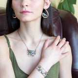 A flashy green labradorite half moon is set inside a brass cup pendant encrusted with oxidized sterling silver coils with pyrite, green kyanite, and citrine gemstone, hanging from a textured darkened sterling silver chain necklace