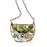 A flashy green labradorite half moon is set inside a brass cup pendant encrusted with oxidized sterling silver coils with pyrite, green kyanite, and citrine gemstone, hanging from a textured darkened sterling silver chain necklace