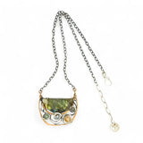 A flashy green labradorite half moon is set inside a brass cup pendant encrusted with oxidized sterling silver coils with pyrite, green kyanite, and citrine gemstone, hanging from a textured darkened sterling silver chain necklace