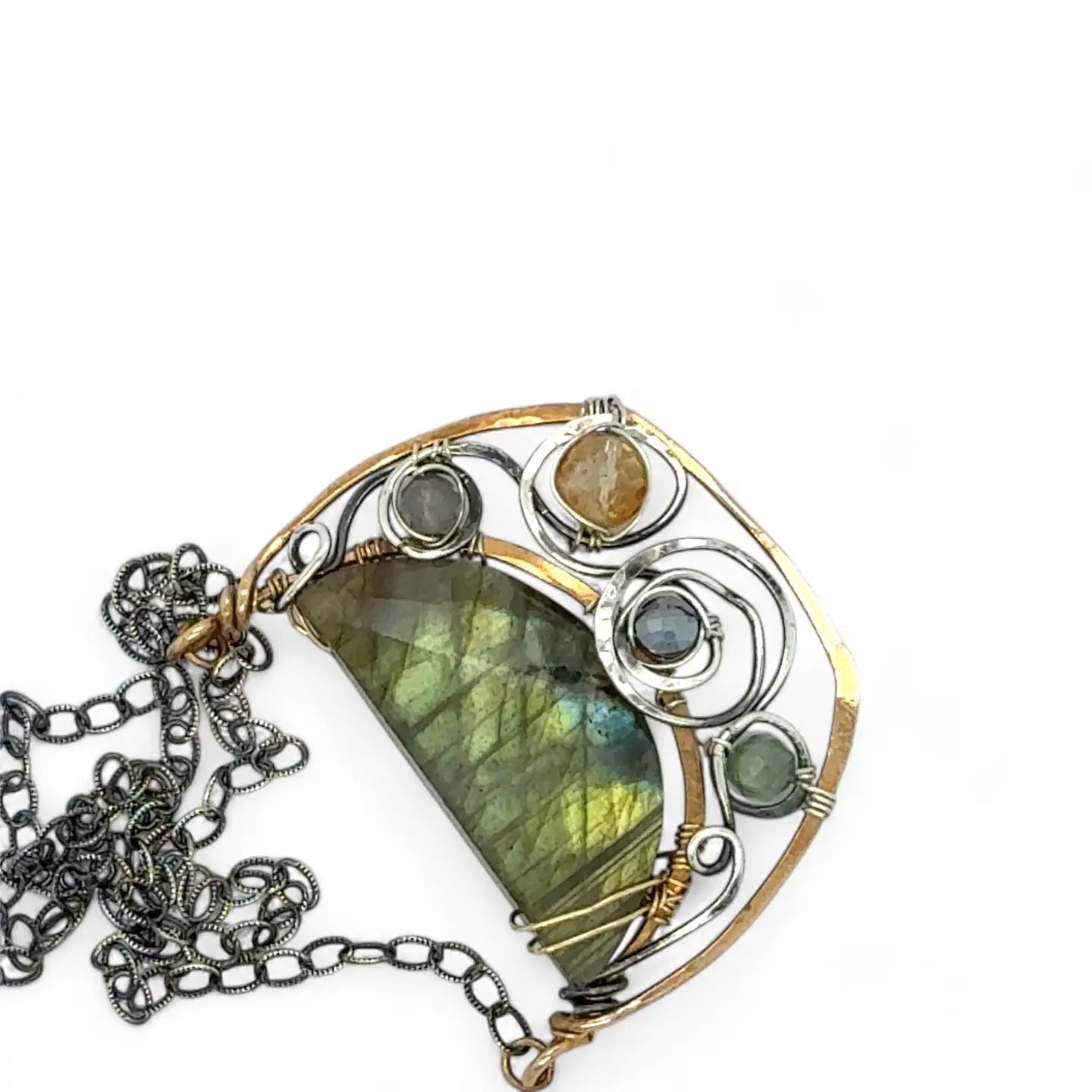 A flashy green labradorite half moon is set inside a brass cup pendant encrusted with oxidized sterling silver coils with pyrite, green kyanite, and citrine gemstone, hanging from a textured darkened sterling silver chain necklace