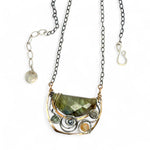 A flashy green labradorite half moon is set inside a brass cup pendant encrusted with oxidized sterling silver coils with pyrite, green kyanite, and citrine gemstone, hanging from a textured darkened sterling silver chain necklace