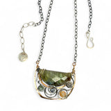 A flashy green labradorite half moon is set inside a brass cup pendant encrusted with oxidized sterling silver coils with pyrite, green kyanite, and citrine gemstone, hanging from a textured darkened sterling silver chain necklace