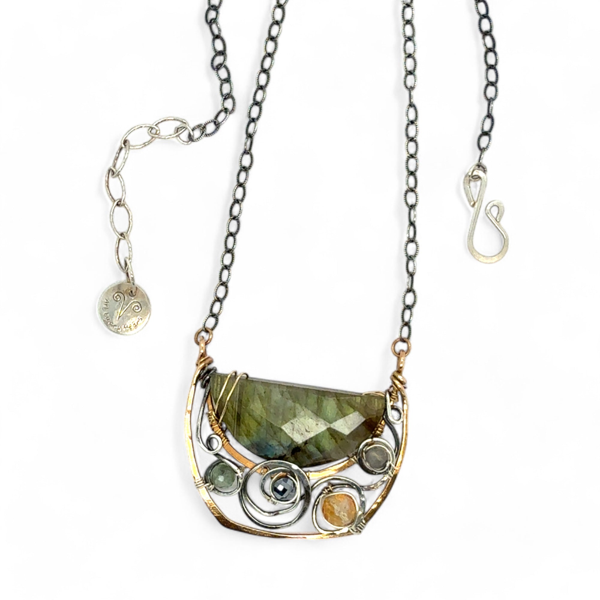 A flashy green labradorite half moon is set inside a brass cup pendant encrusted with oxidized sterling silver coils with pyrite, green kyanite, and citrine gemstone, hanging from a textured darkened sterling silver chain necklace