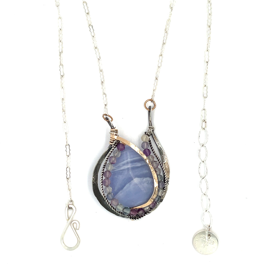 A blue lace agate drop pendant necklace with faceted natural fluorite gemstones, set in hammered bronze and twisted oxidized sterling silver, on a darkened floral stamped sterling silver pendant