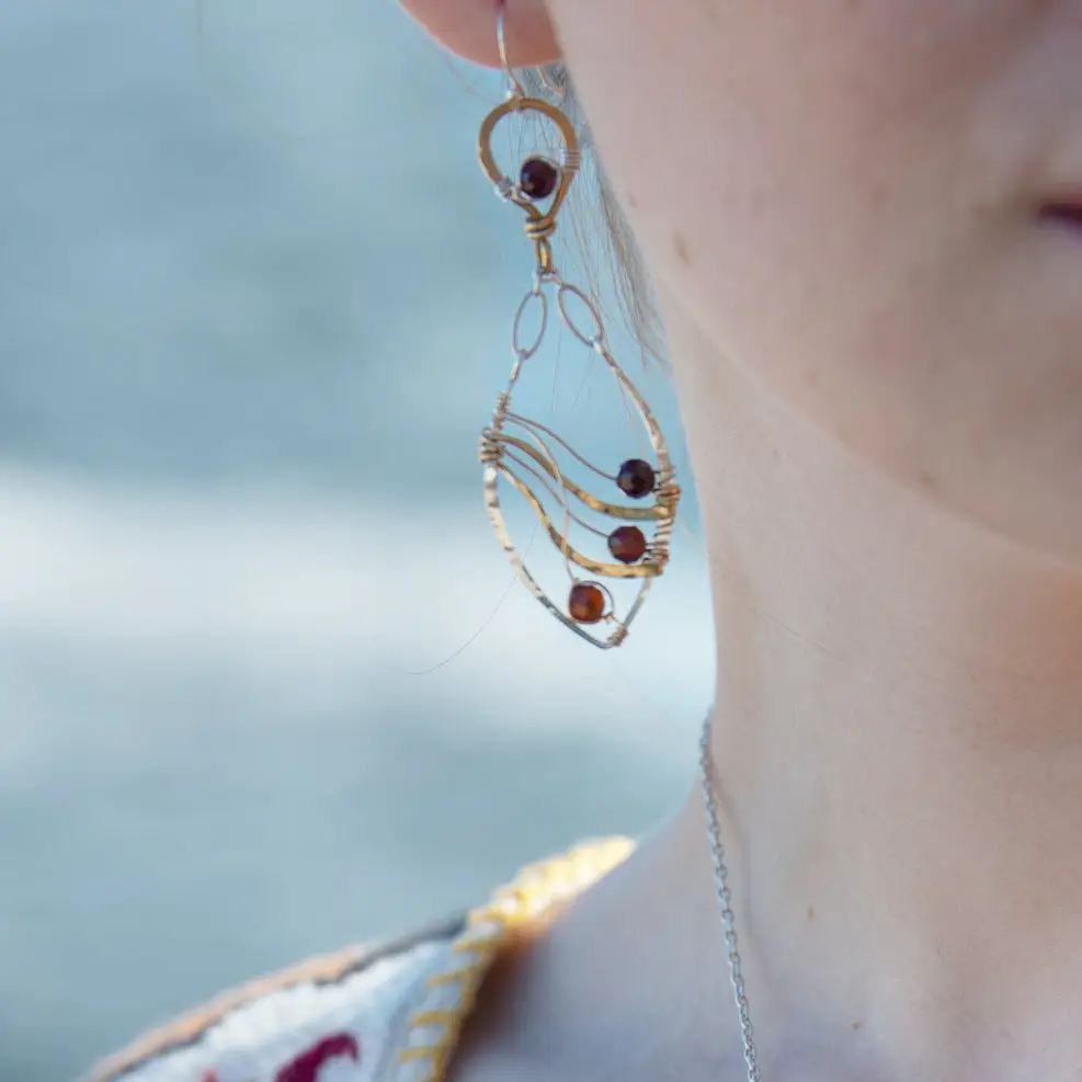 A pair of gold-filled, hammered brass and sterling silver earrings with faceted hessonite garnet gemstones, featuring sterling silver french hooks.