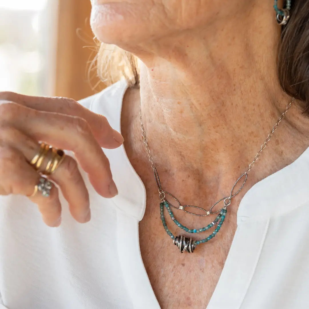 A sterling silver oxidized knot is set on layers of bright blue apatite gemstones with silver crystal cube accents, oxidized sterling diamond cut links and a dainty sterling chain necklace 