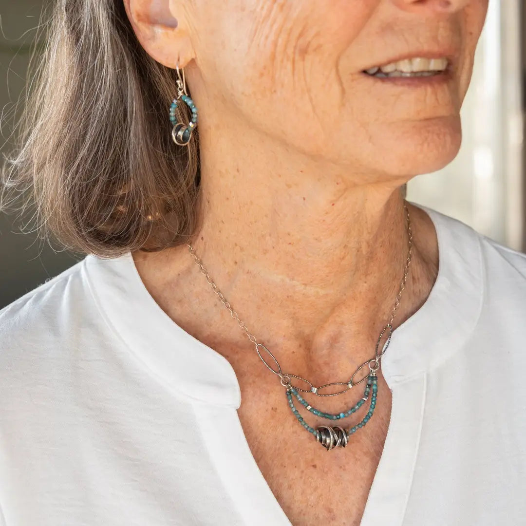 A sterling silver oxidized knot is set on layers of bright blue apatite gemstones with silver crystal cube accents, oxidized sterling diamond cut links and a dainty sterling chain necklace 