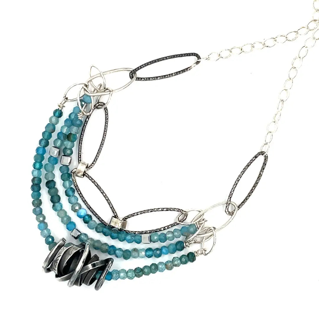 A sterling silver oxidized knot is set on layers of bright blue apatite gemstones with silver crystal cube accents, oxidized sterling diamond cut links and a dainty sterling chain necklace 