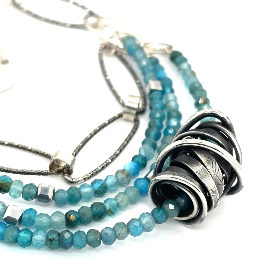 A sterling silver oxidized knot is set on layers of bright blue apatite gemstones with silver crystal cube accents, oxidized sterling diamond cut links and a dainty sterling chain necklace 