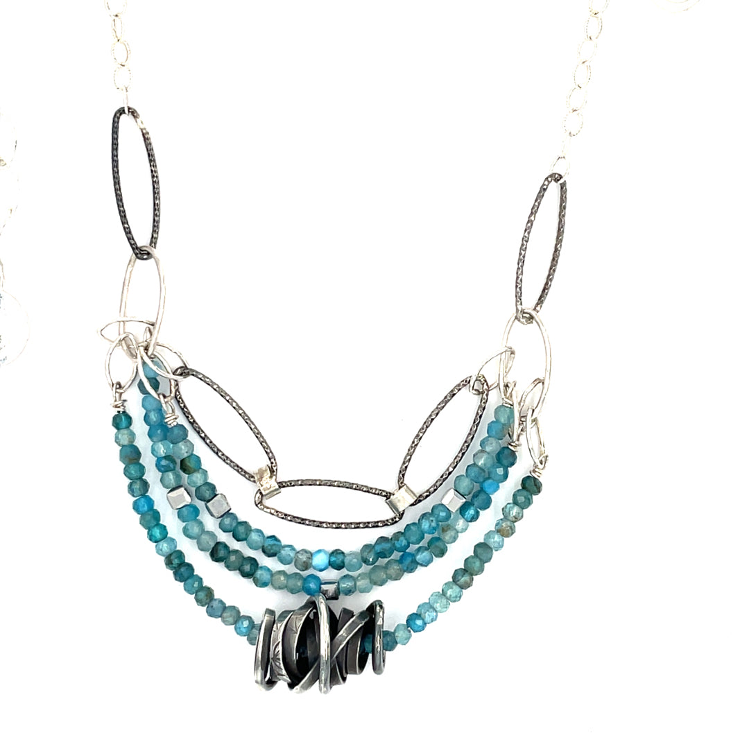 A sterling silver oxidized knot is set on layers of bright blue apatite gemstones with silver crystal cube accents, oxidized sterling diamond cut links and a dainty sterling chain necklace 