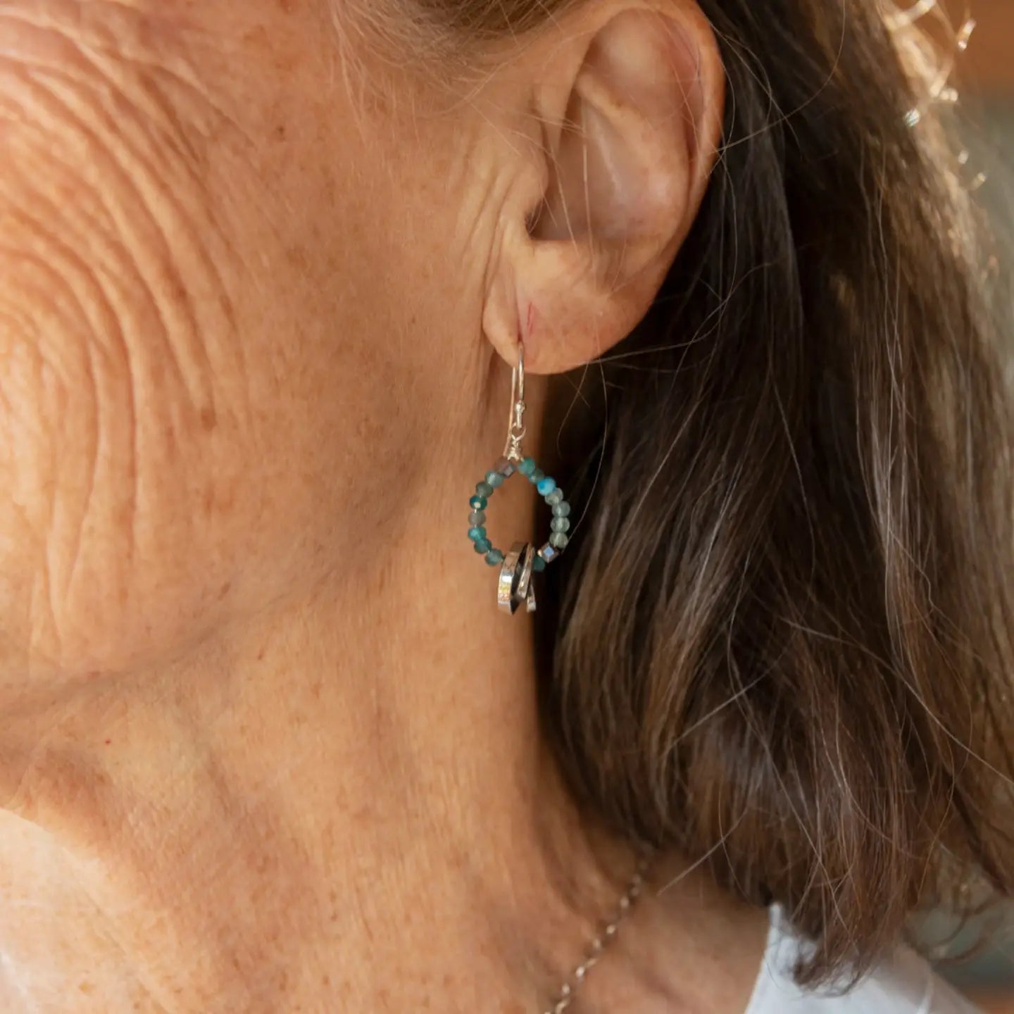 Faceted apatite gemstones form a ring that holds onto and oxidized sterling silver hand formed knot earring