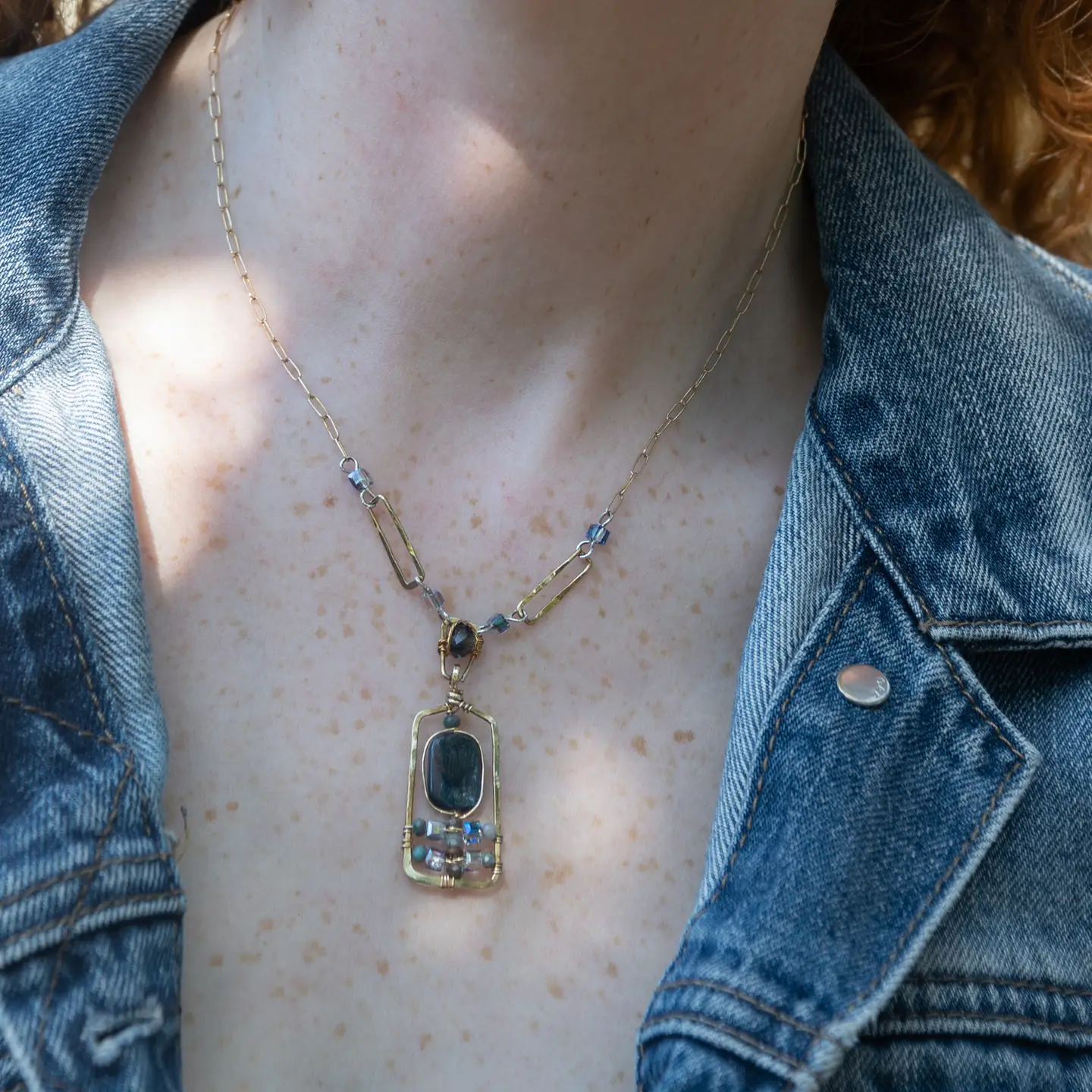 Smooth kyanite accented with crystal cubes and blue tourmaline gemstones inside a brass rectangle hanging from handmade hammered brass rectangle link necklace