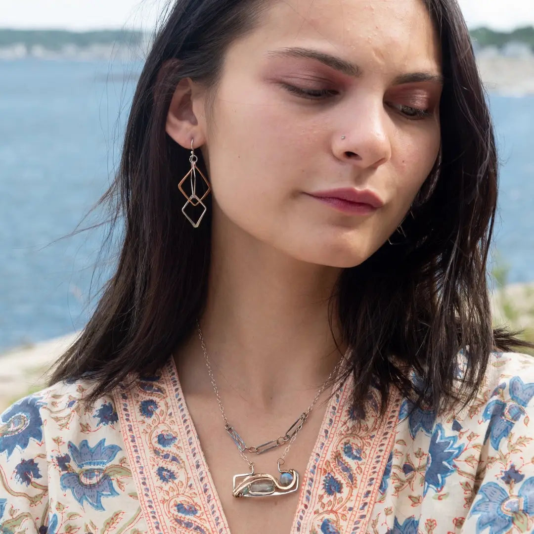 A double-layered necklace with a geometric design, featuring a rectangular darkened sterling silver pendant with a fluorite gemstone, flashy labradorite gemstone, and bronze accents, connected to chain links and additional bronze rings.