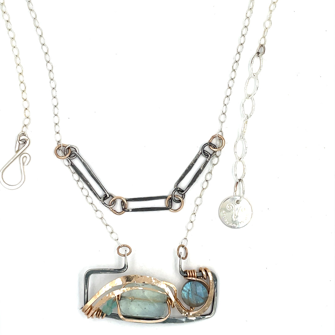 A double-layered necklace with a geometric design, featuring a rectangular darkened sterling silver pendant with a fluorite gemstone, flashy labradorite gemstone, and bronze accents, connected to chain links and additional bronze rings.