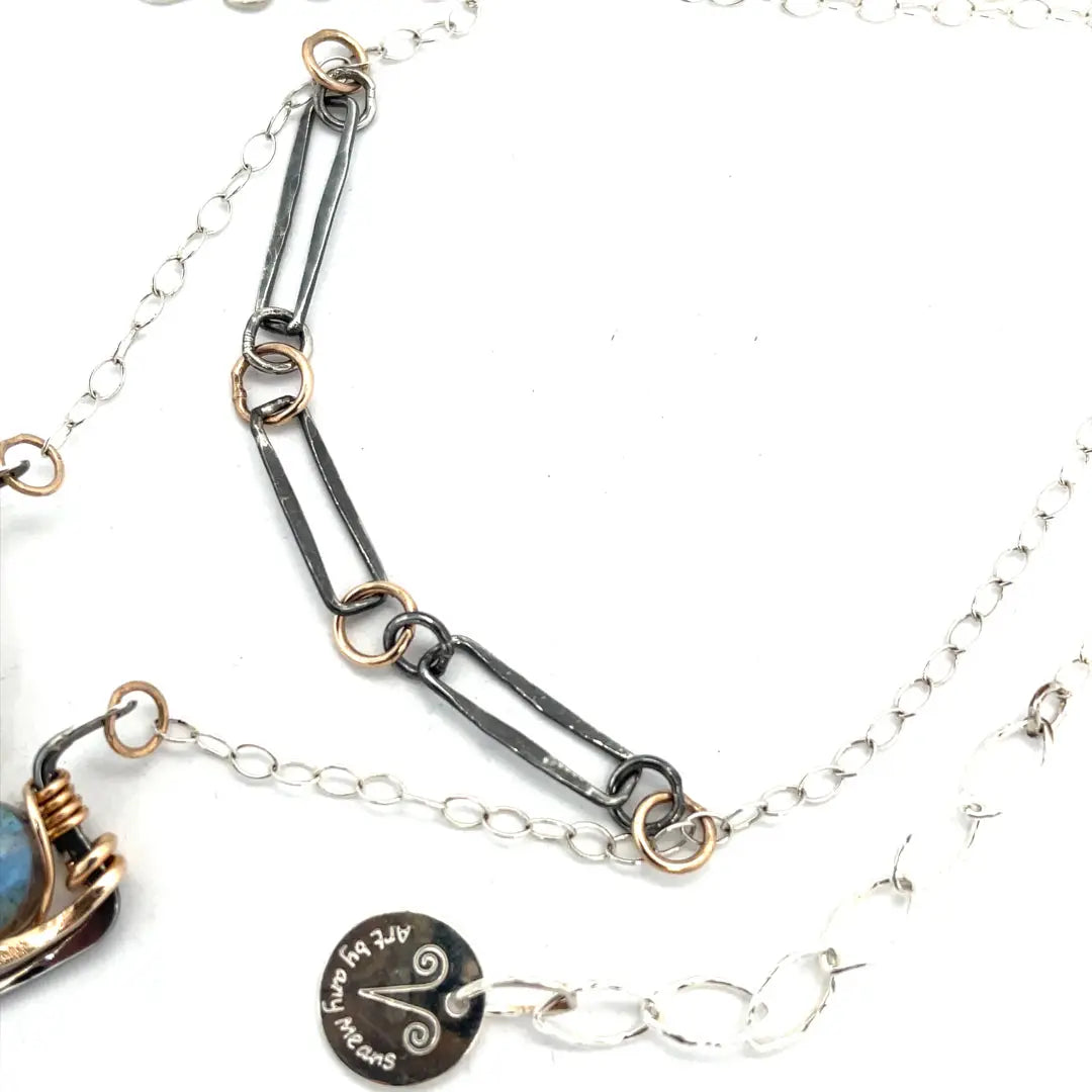 A double-layered necklace with a geometric design, featuring a rectangular darkened sterling silver pendant with a fluorite gemstone, flashy labradorite gemstone, and bronze accents, connected to chain links and additional bronze rings.
