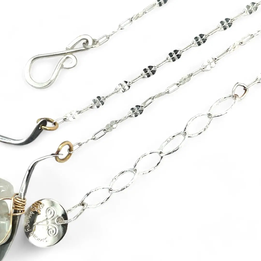 A darkened sterling silver moth-shaped pendant featuring a smooth cream agate gemstone, white sapphire, and jade drops, complemented by a fresh water pearl, with layers of gold filled and hammered brass wires