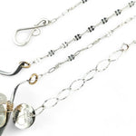 A darkened sterling silver moth-shaped pendant featuring a smooth cream agate gemstone, white sapphire, and jade drops, complemented by a fresh water pearl, with layers of gold filled and hammered brass wires