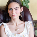 A darkened sterling silver moth-shaped pendant featuring a smooth cream agate gemstone, white sapphire, and jade drops, complemented by a fresh water pearl, with layers of gold filled and hammered brass wires