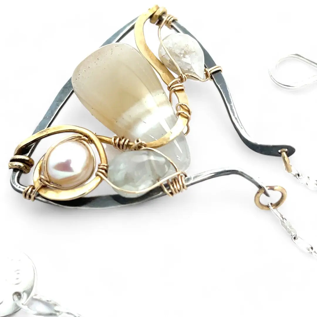 A darkened sterling silver moth-shaped pendant featuring a smooth cream agate gemstone, white sapphire, and jade drops, complemented by a fresh water pearl, with layers of gold filled and hammered brass wires