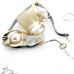 A darkened sterling silver moth-shaped pendant featuring a smooth cream agate gemstone, white sapphire, and jade drops, complemented by a fresh water pearl, with layers of gold filled and hammered brass wires