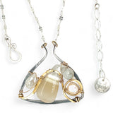 A darkened sterling silver moth-shaped pendant featuring a smooth cream agate gemstone, white sapphire, and jade drops, complemented by a fresh water pearl, with layers of gold filled and hammered brass wires