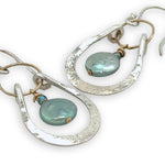 Mint fresh water pearl coin held within a stamped and hammered sterling silver open hoop hanging on a gold filled braided link