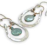 Mint fresh water pearl coin held within a stamped and hammered sterling silver open hoop hanging on a gold filled braided link