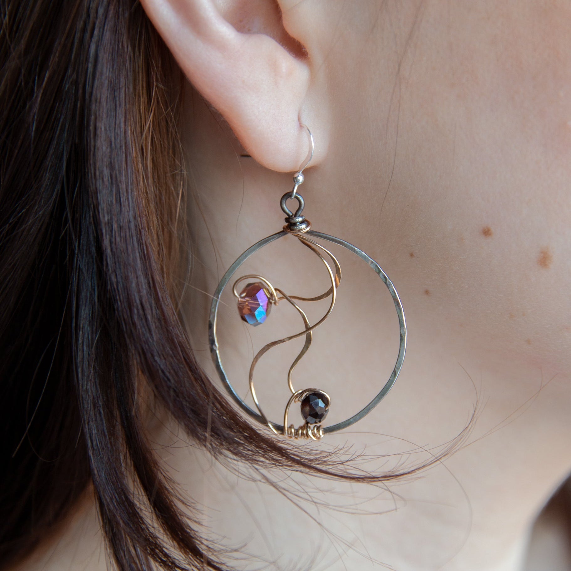 Darkened sterling silver hoop earrings with pink/purple crystals held in rivers of hammered bronze wire