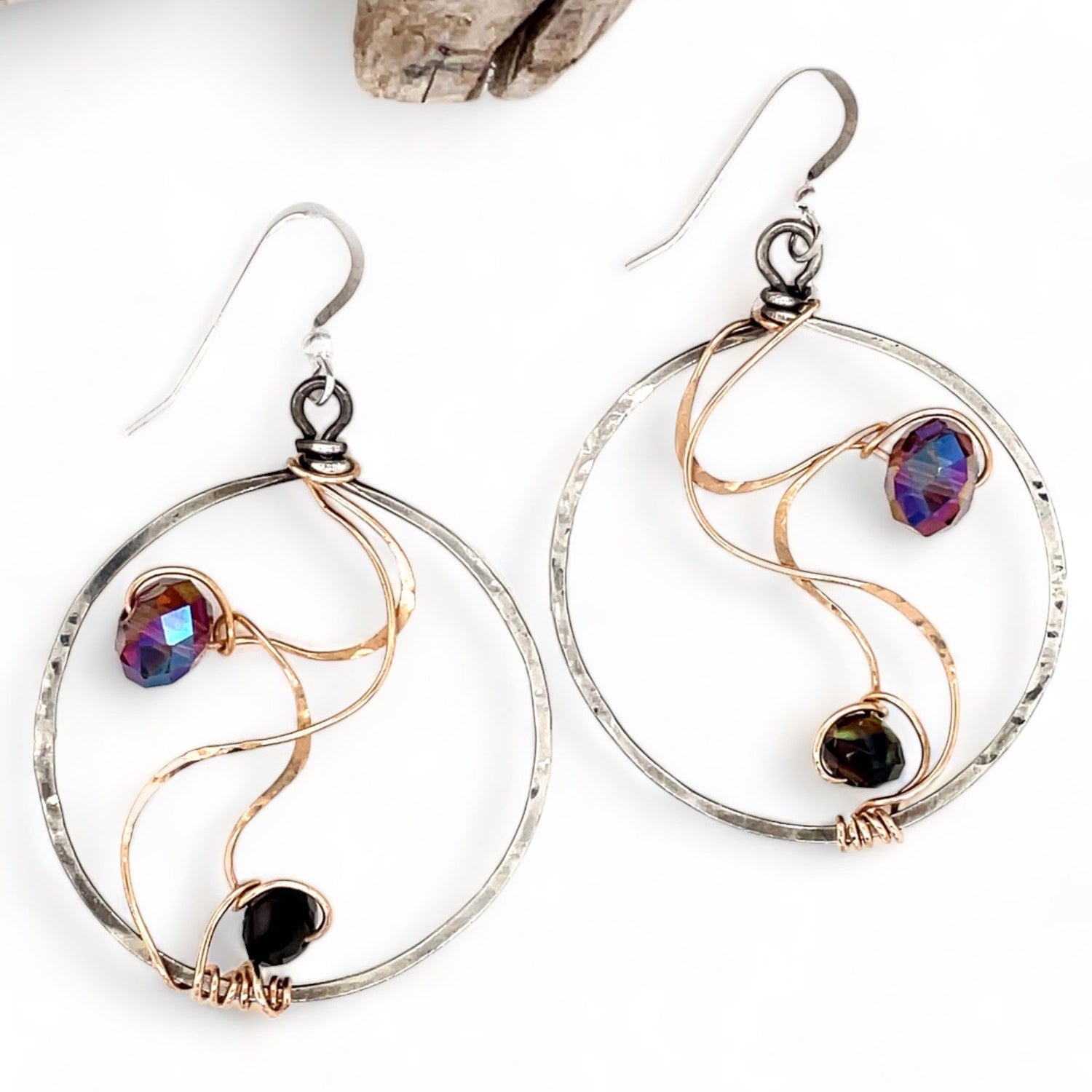 Darkened sterling silver hoop earrings with pink/purple crystals held in rivers of hammered bronze wire