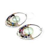 A pair of sterling silver hoop earringsthat have been stamped with dandelions and swirls, featuring a green fluorite smooth coin wrapped in gold filled wire and surrounded by a array of multicolored gemstones.