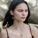 A pair of sterling silver hoop earringsthat have been stamped with dandelions and swirls, featuring a green fluorite smooth coin wrapped in gold filled wire and surrounded by a array of multicolored gemstones.