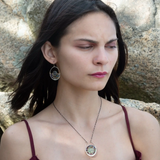 A pair of sterling silver hoop earringsthat have been stamped with dandelions and swirls, featuring a green fluorite smooth coin wrapped in gold filled wire and surrounded by a array of multicolored gemstones.