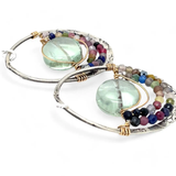 A pair of sterling silver hoop earringsthat have been stamped with dandelions and swirls, featuring a green fluorite smooth coin wrapped in gold filled wire and surrounded by a array of multicolored gemstones.