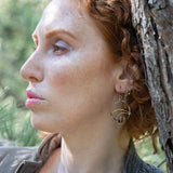 A pair of earrings featuring gestural knots of hand-formed hammered brass on oxidized sterling silver hoops