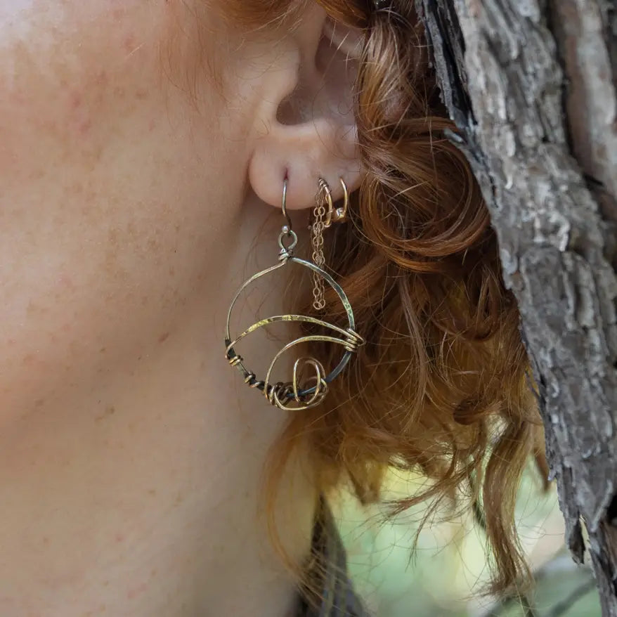 A pair of earrings featuring gestural knots of hand-formed hammered brass on oxidized sterling silver hoops