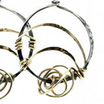 A pair of earrings featuring gestural knots of hand-formed hammered brass on oxidized sterling silver hoops