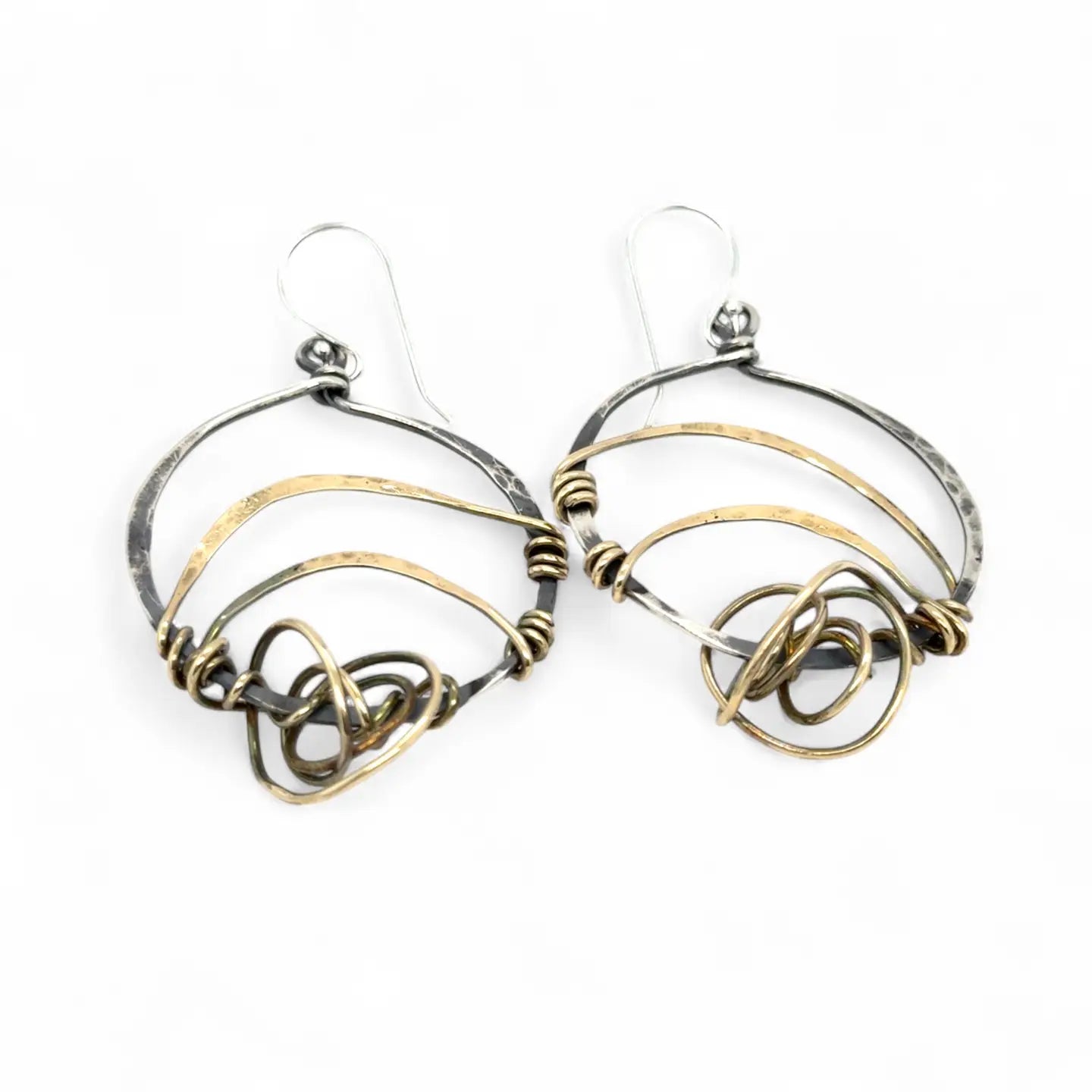 A pair of earrings featuring gestural knots of hand-formed hammered brass on oxidized sterling silver hoops